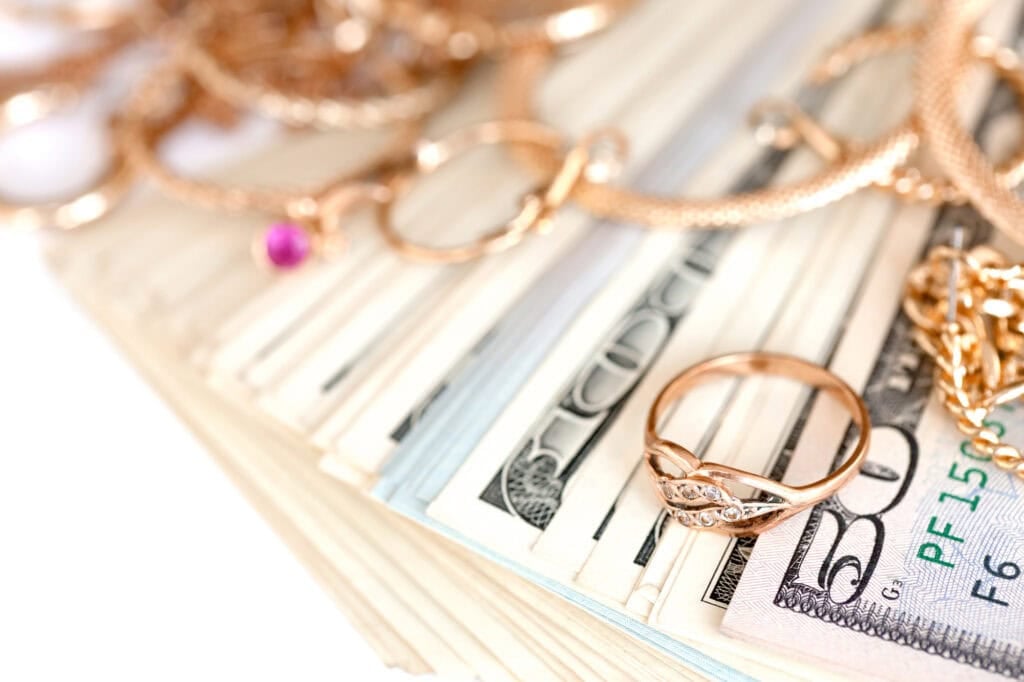 Many gold jewelry rings, earrings and necklaces with big amount of US dollar bills on white background. How To Sell Gold (Step-By-Step Guide)
